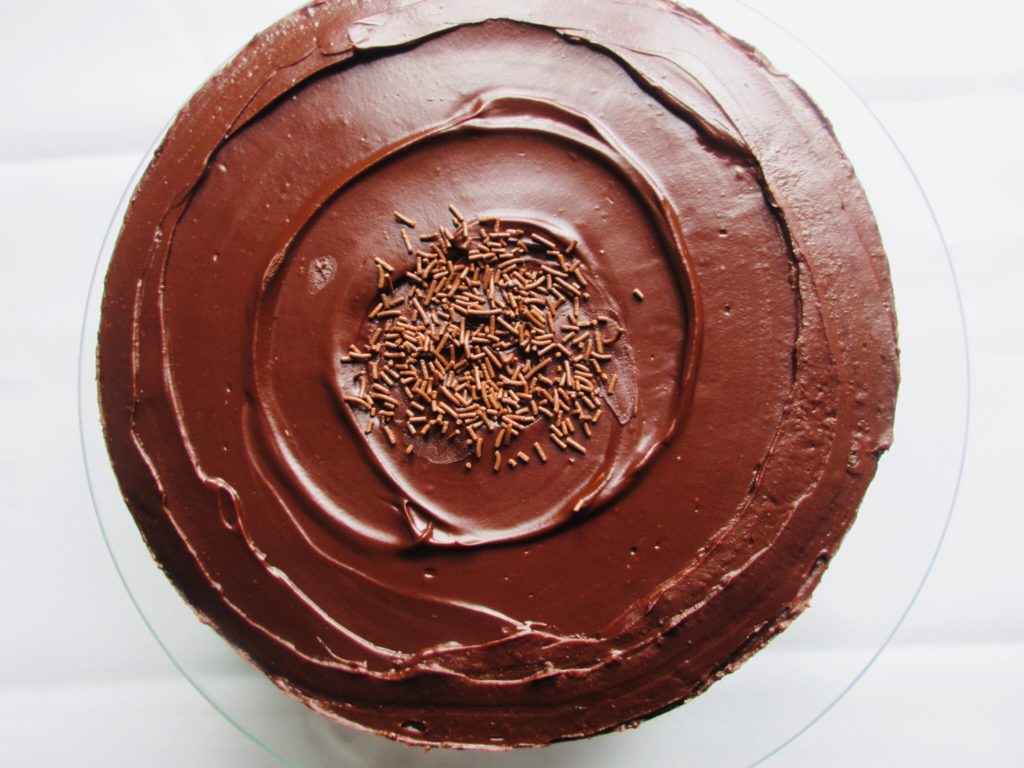 Top view of a chocolate cake covered with chocolate ganache and chocolate sprinkles in the middle. 