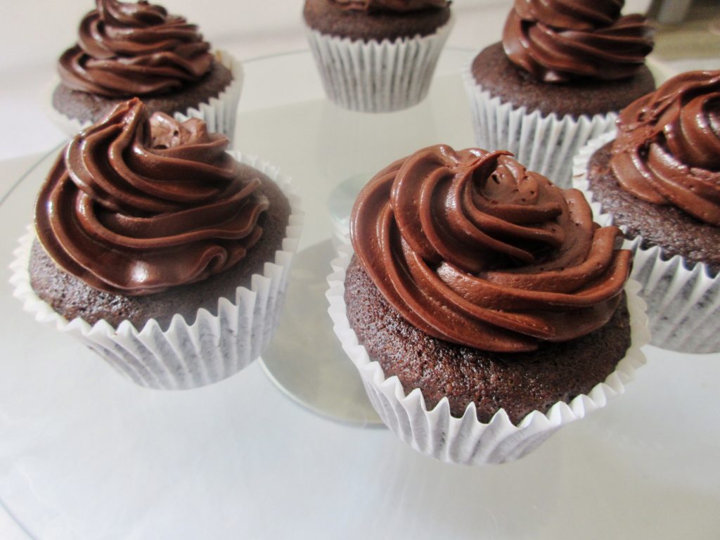 Double chocolate cupcakes with whipped ganache frosting on a glass cake turntable.