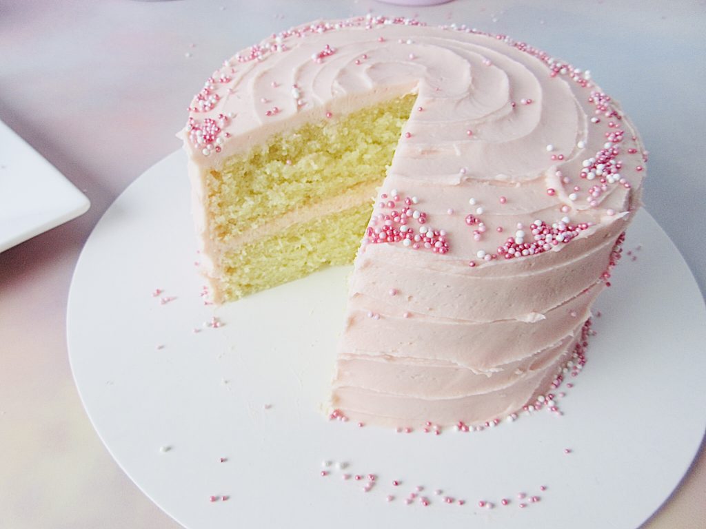 Small vanilla cake with pink frosting and a slice cut from it.