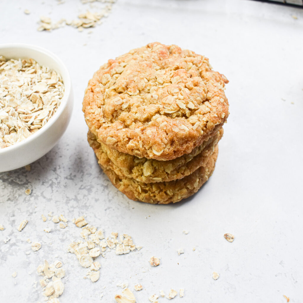 3 oat cookies stacked to the left of the stack is a small white bowl with raw oats.