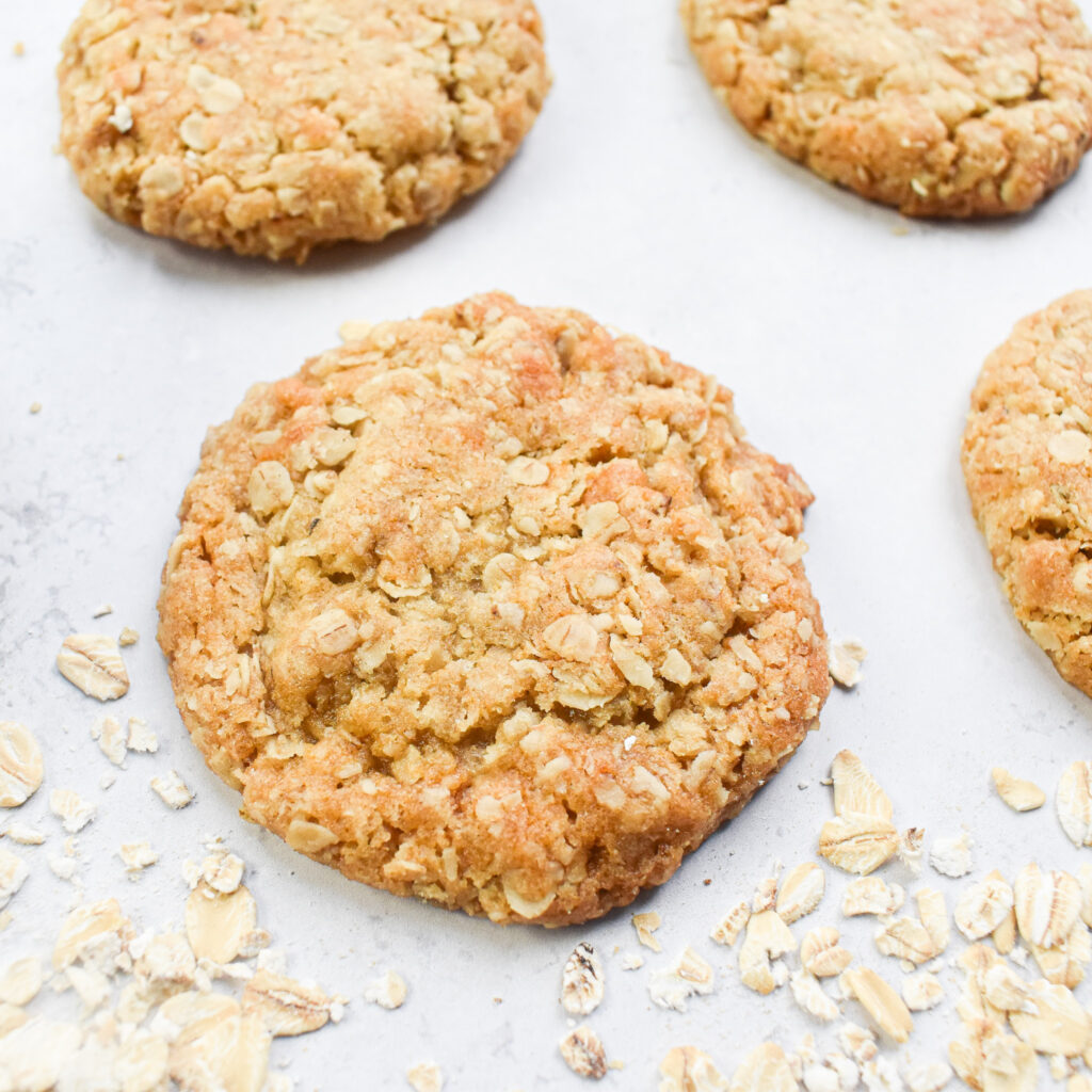 Oat biscuits laid out on a flat surface with oats sprinkle around one of them.