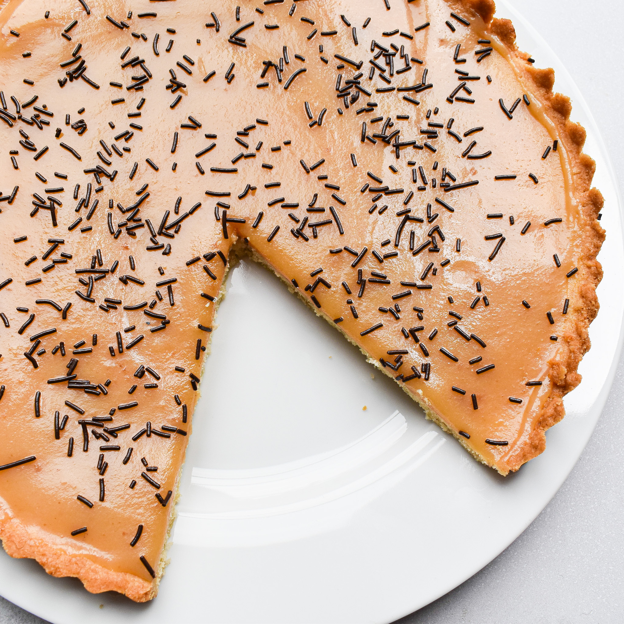Caramel tart on a white plate with a slice cut out.