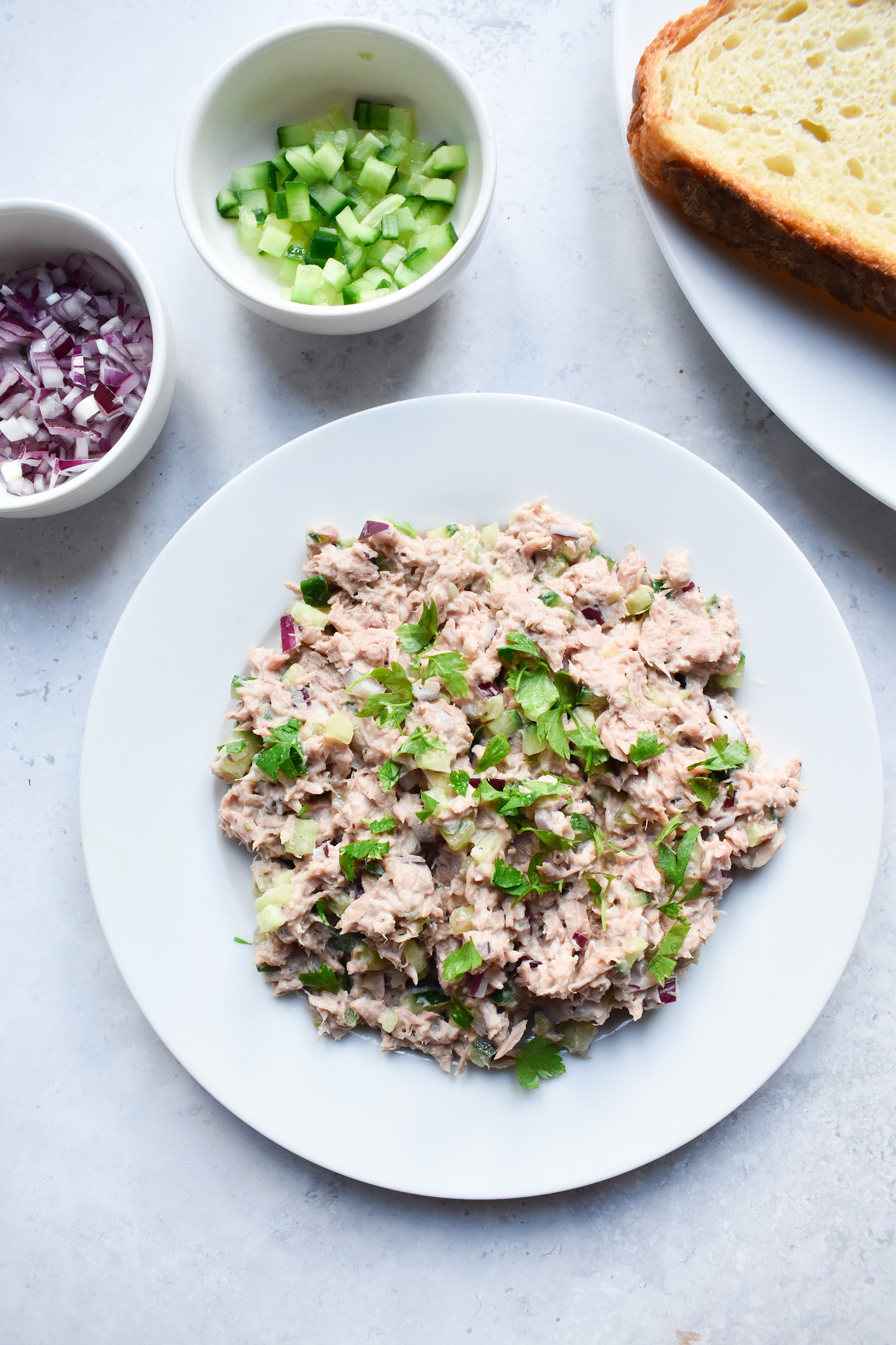 Tuna crunch filling on a white plate with small pot of chopped cucumbers in background.