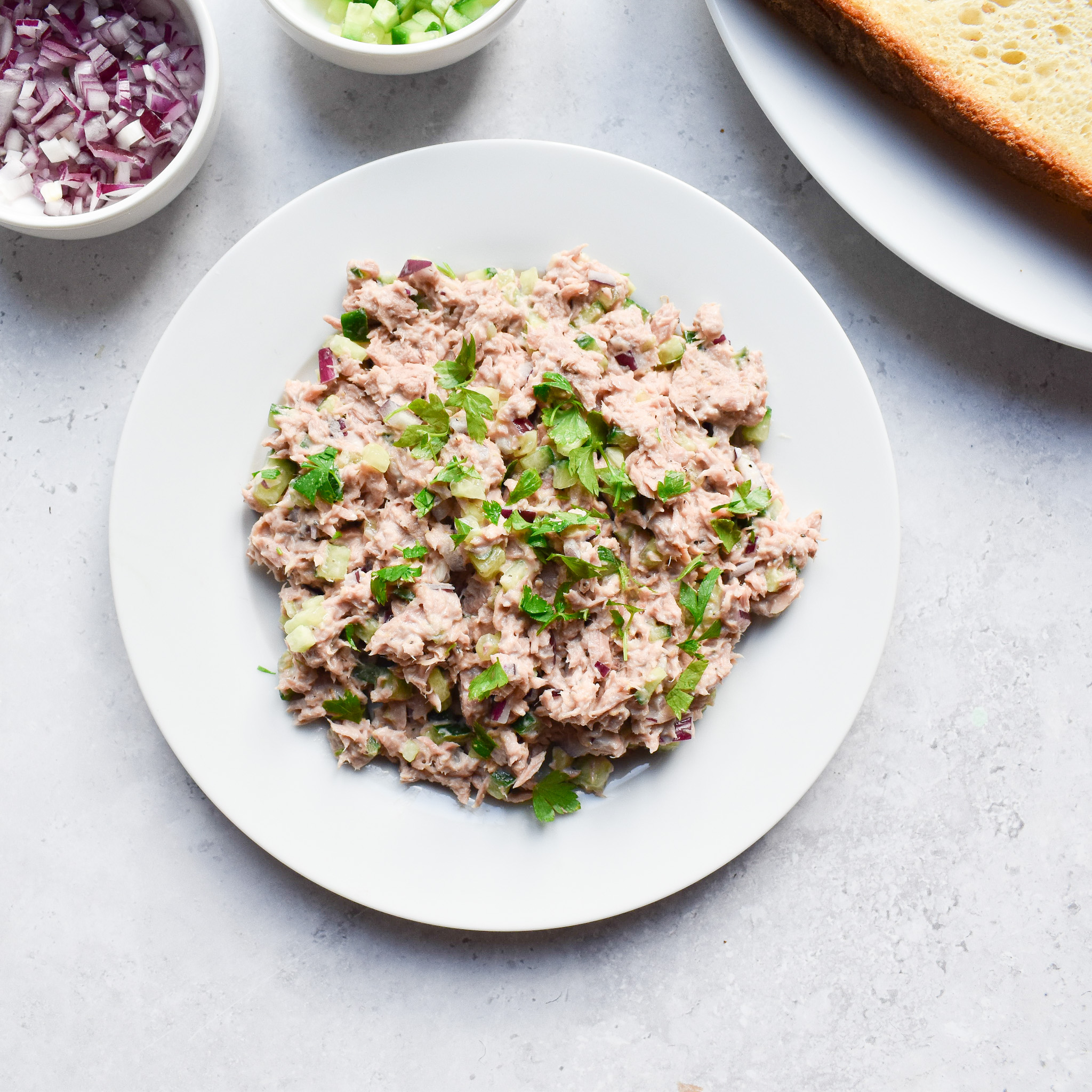 Tuna crunch filling on a white plate with small pot of chopped red onion in background.