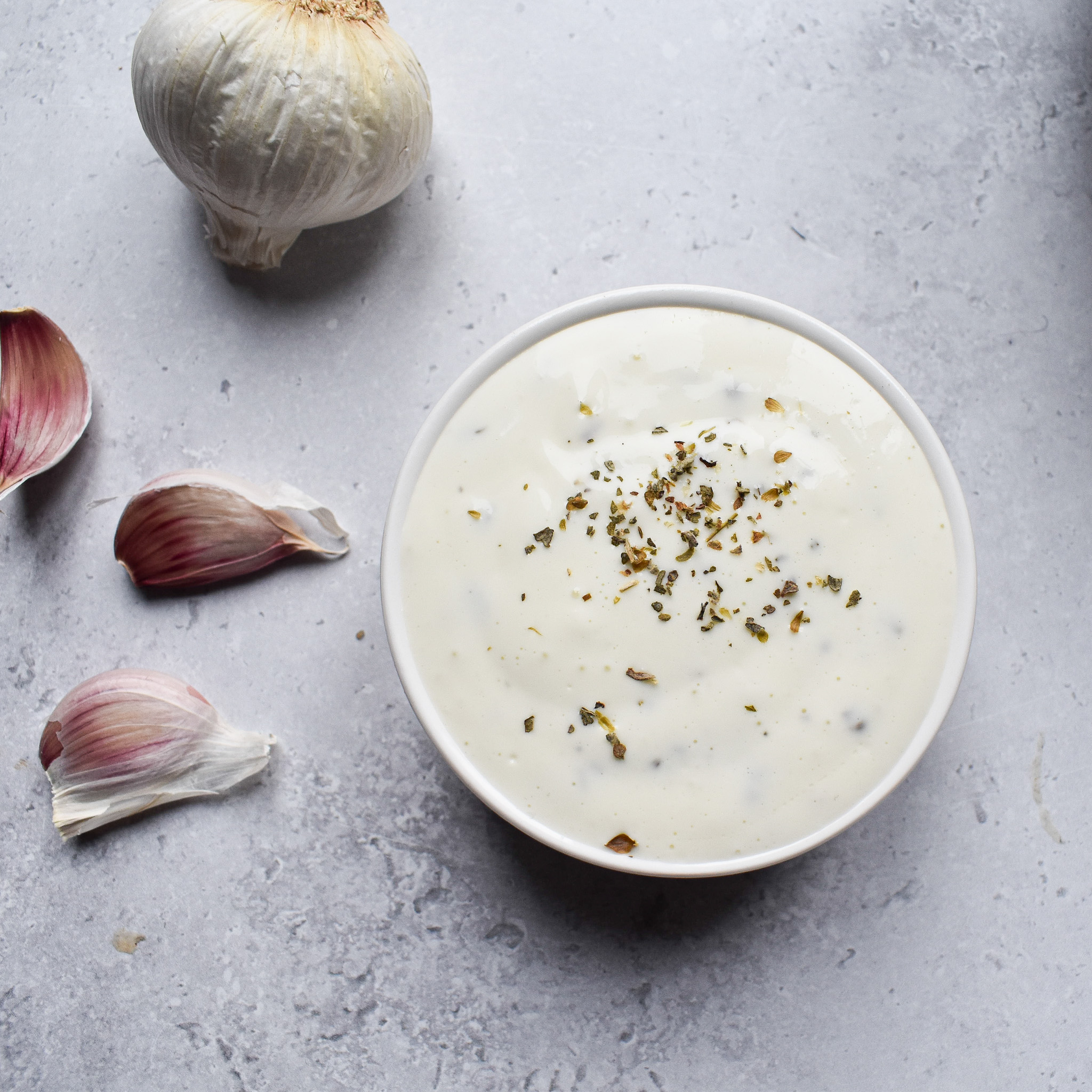 Garlic yoghurt sauce in a bowl with garlic cloves next to it.
