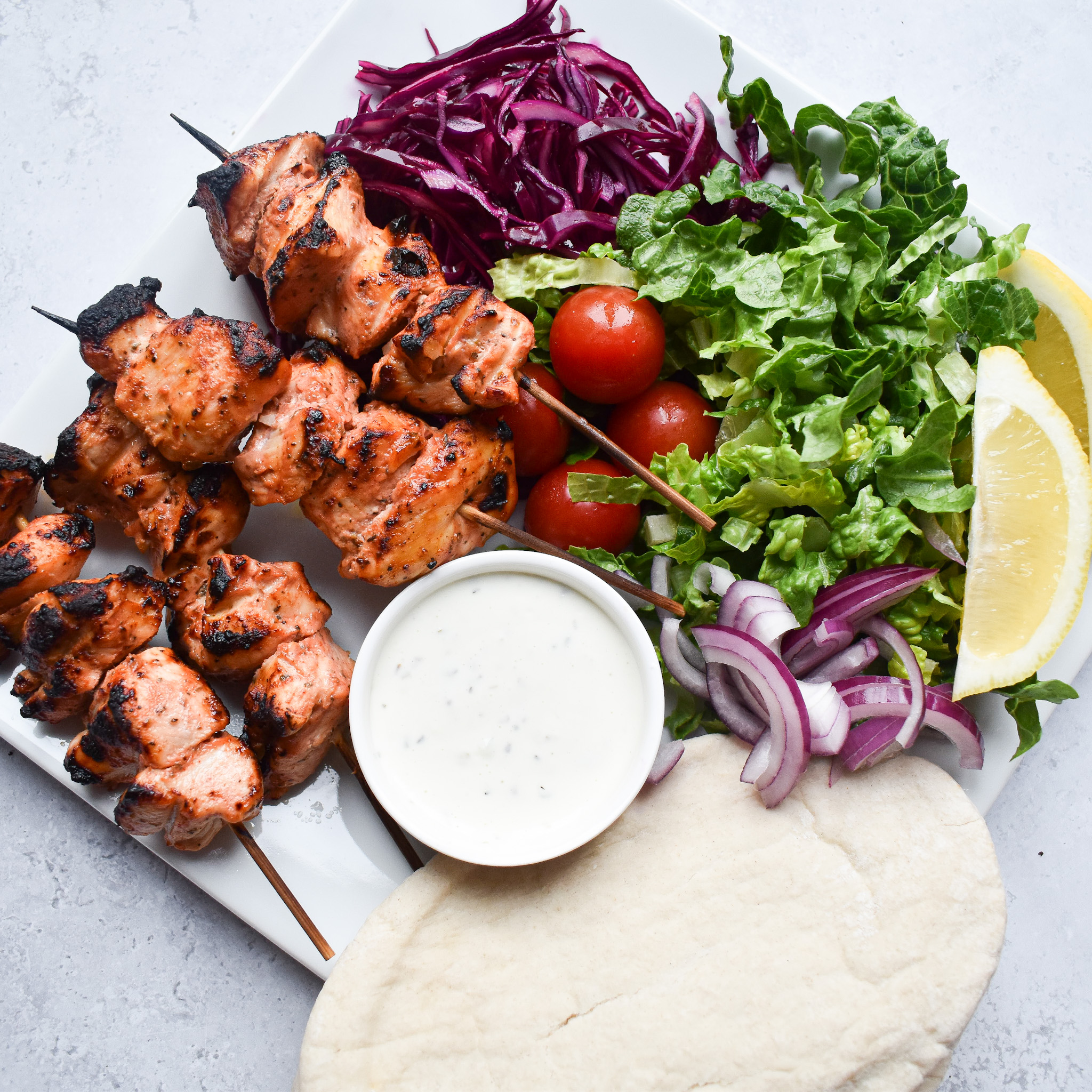 Chicken shish kebabs on a plate with salad and a pot of sauce with a pitta bread