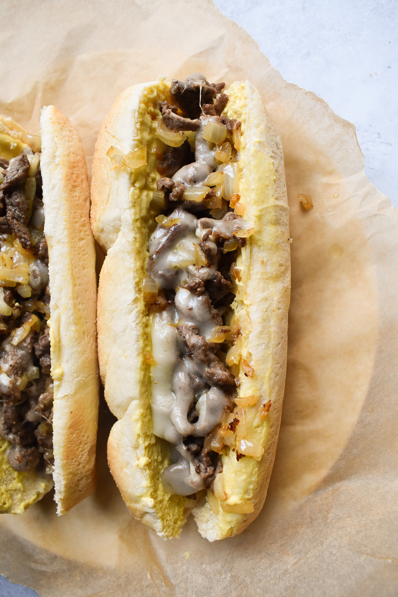 cheesesteak sandwiches on brown parchment paper.