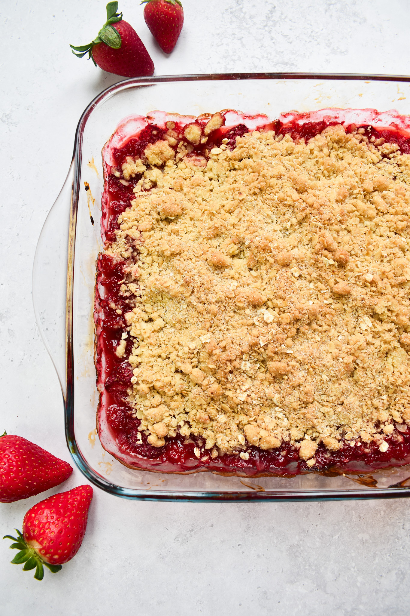 Strawberry crumble in clear dish with strawberries for decoration.