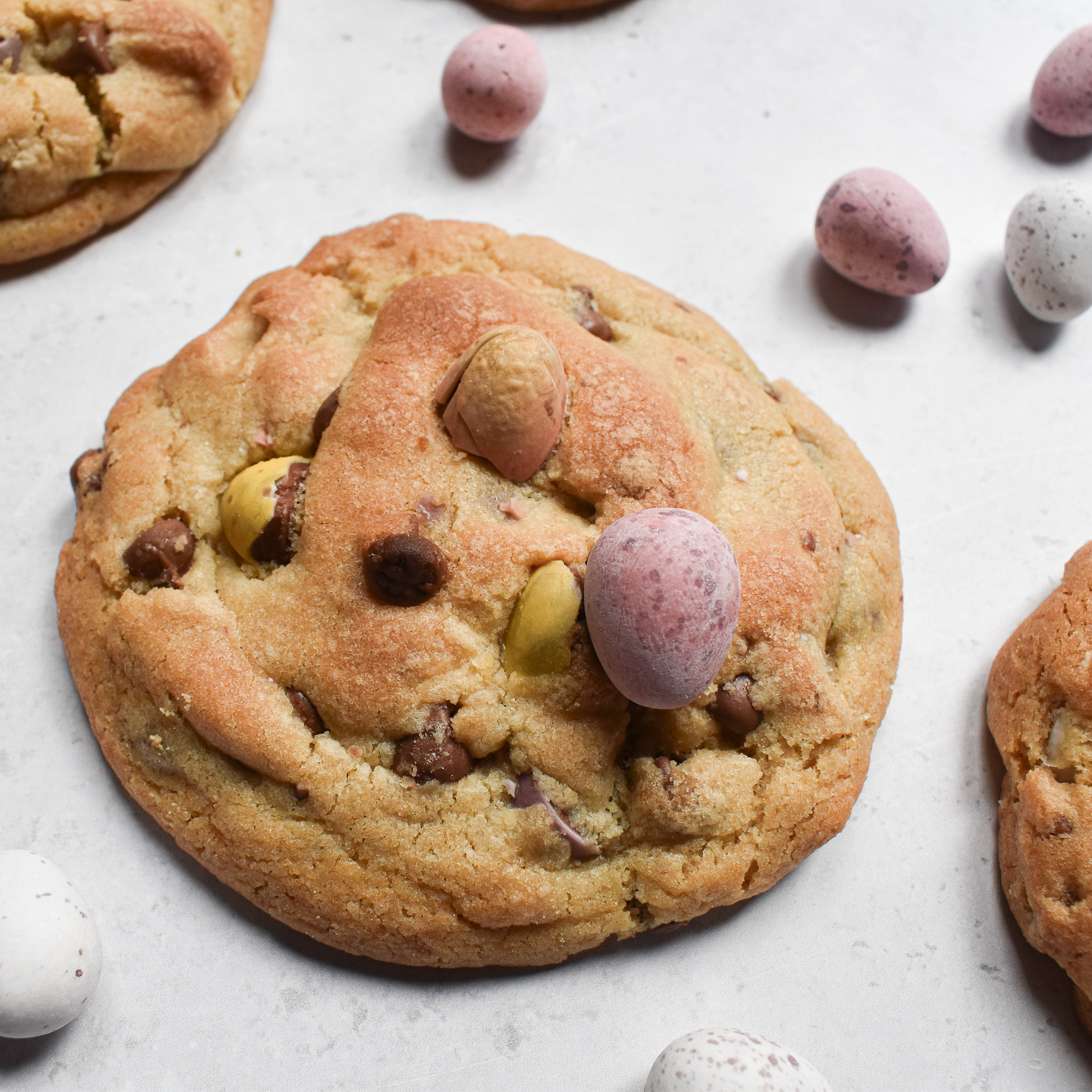 1 chunky mini egg cookies with a few mini eggs scattered around it.