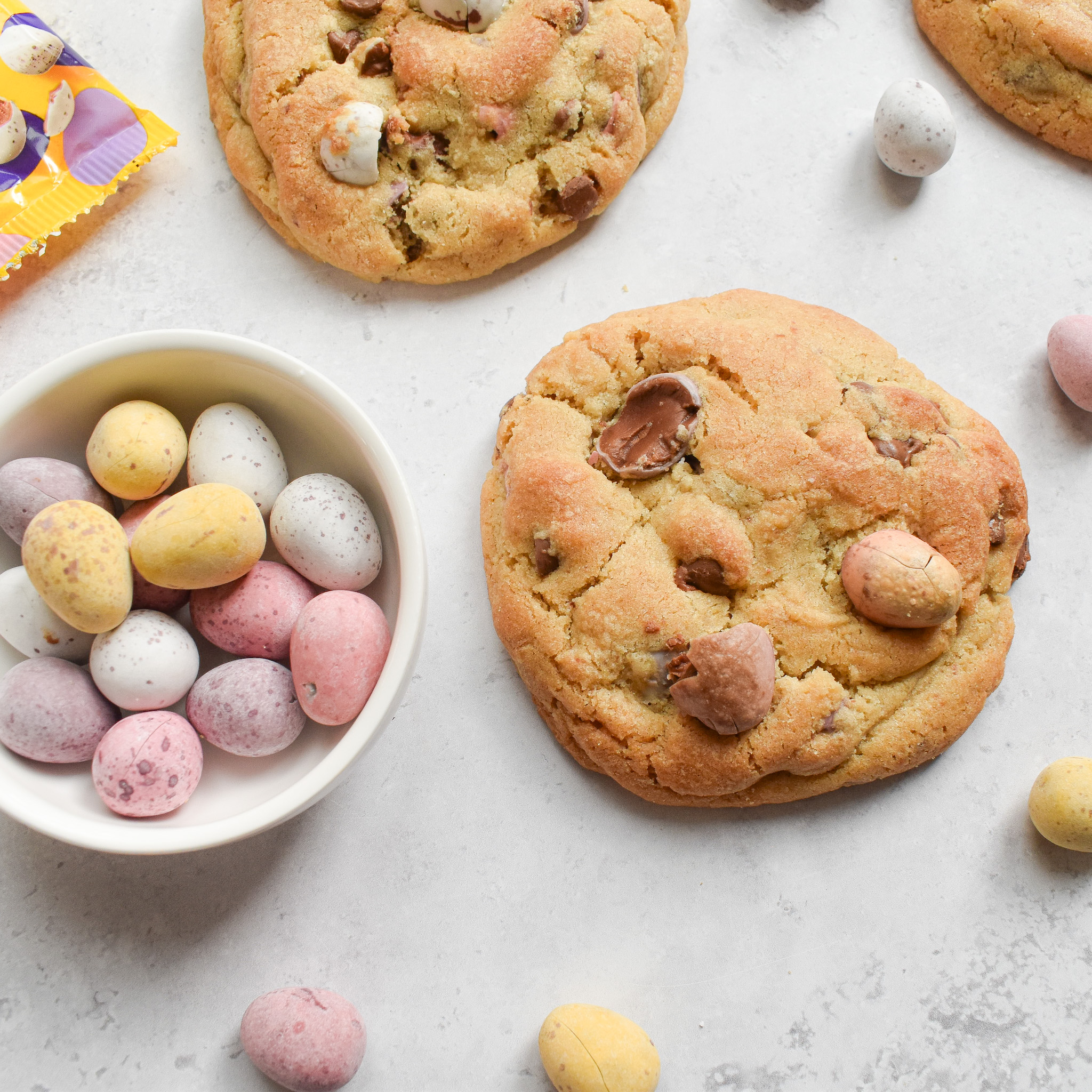 Mini egg cookies next to a small white bowl that contains mini eggs.
