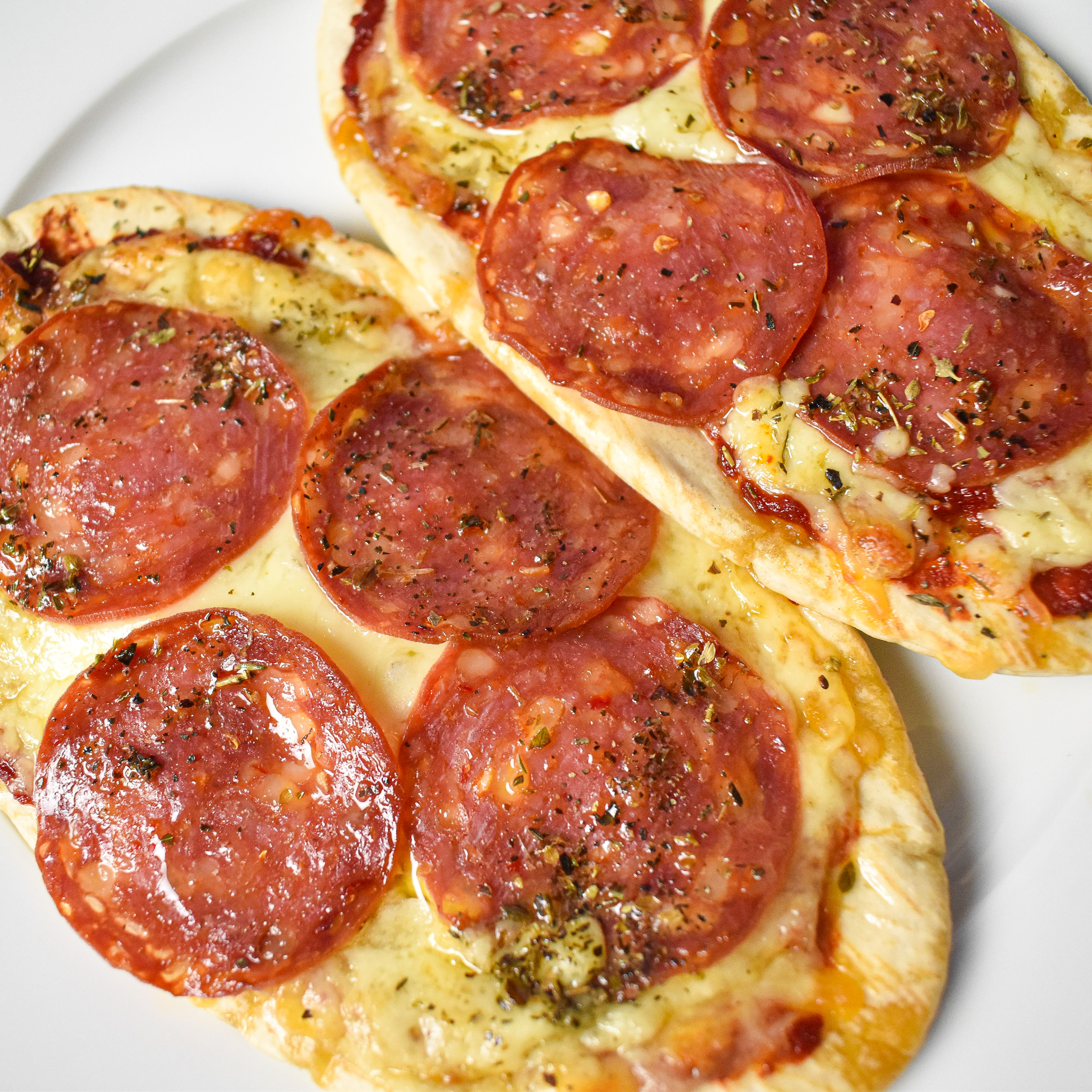 2 pepperoni pitta pizzas on a white plate.