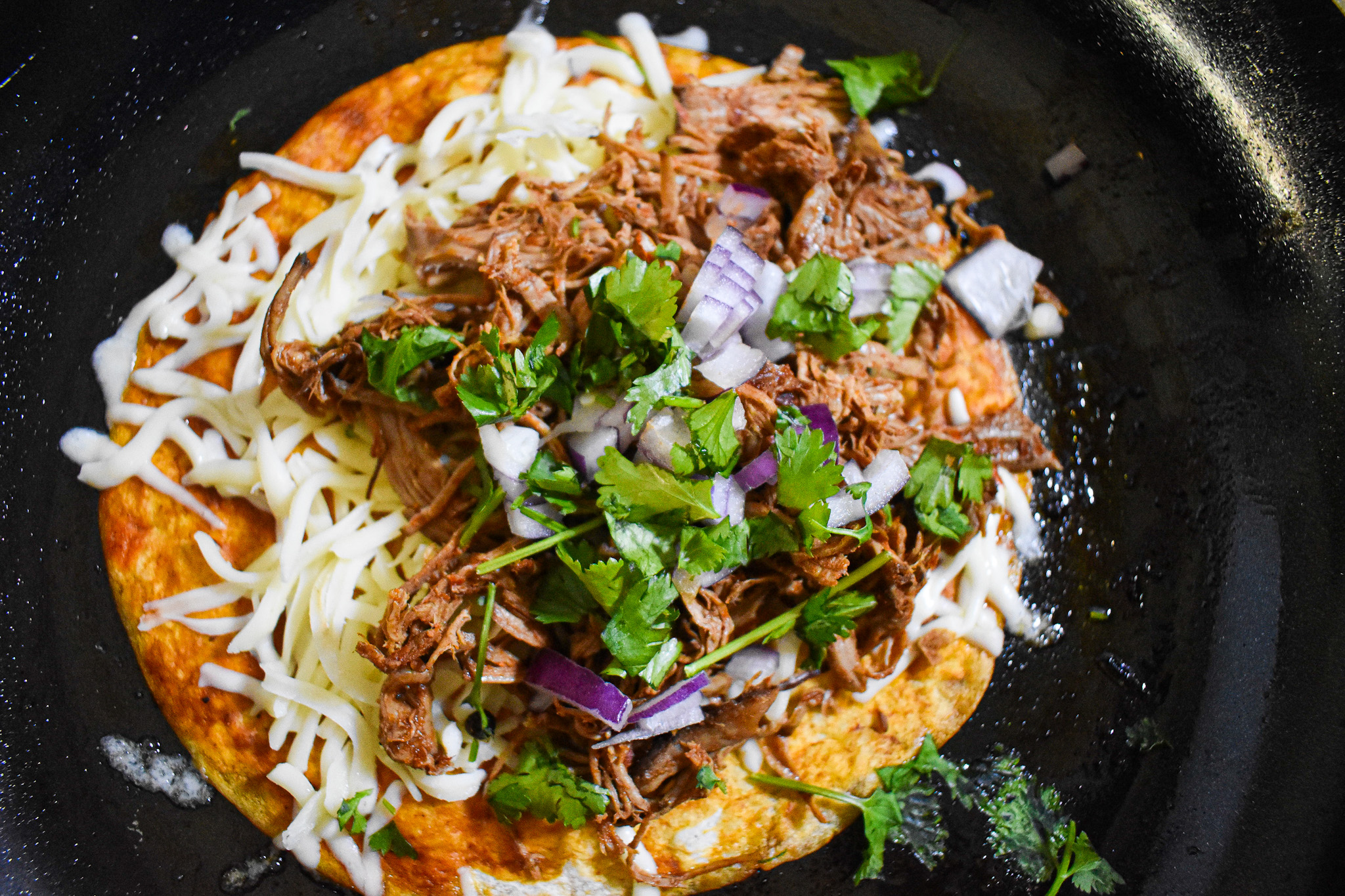 showing how to assemble birria tacos in a frying pan.