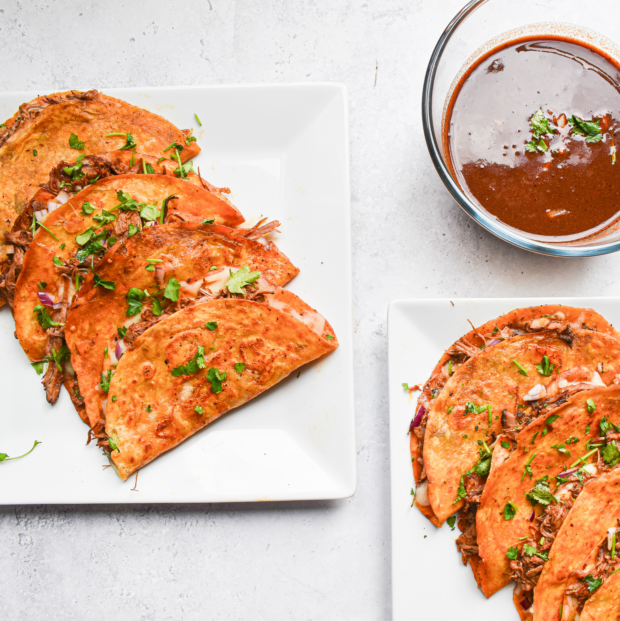 2 white plates with 4 tacos on each plate and a bowl with spicy sauce.