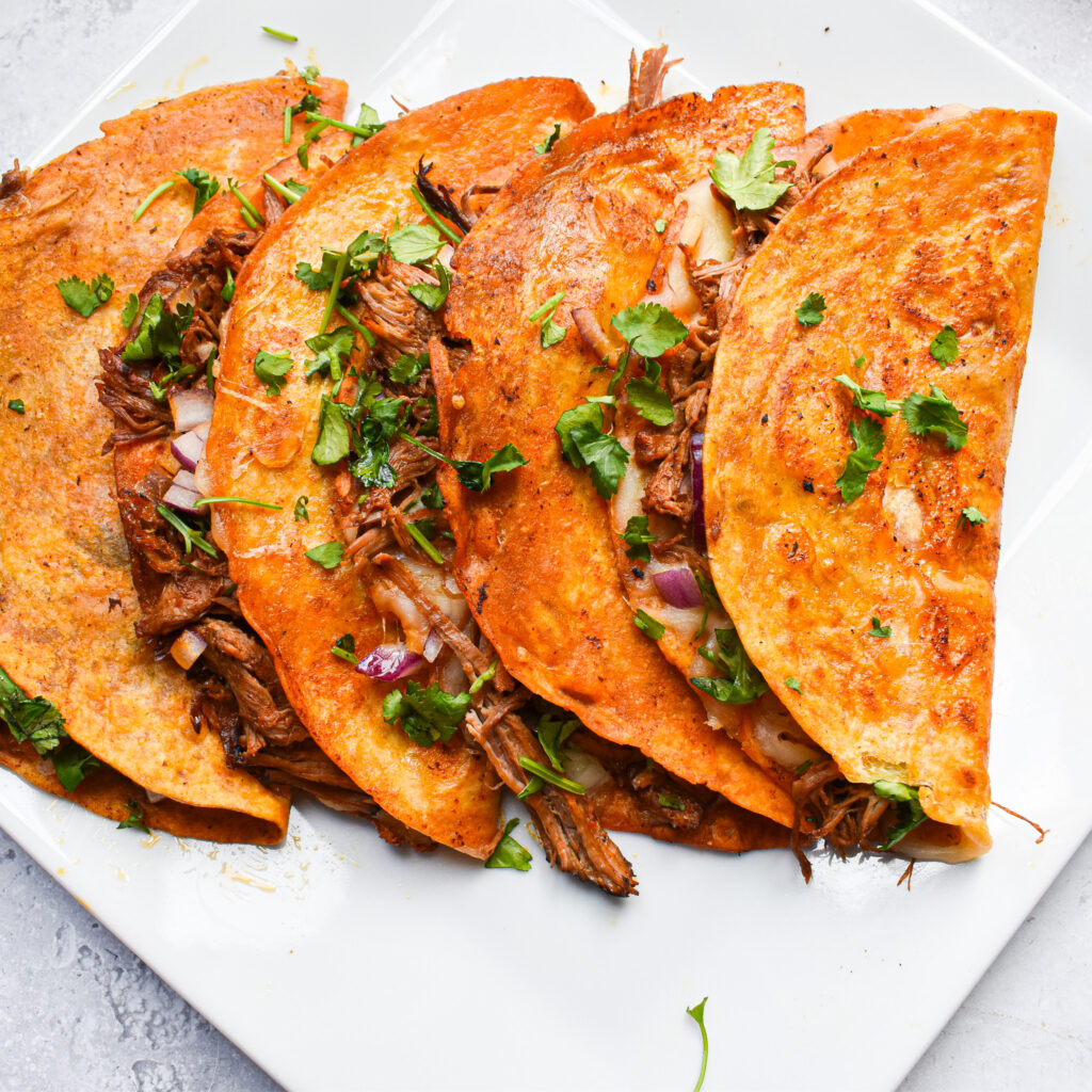 4 birria tacos on a white plate.