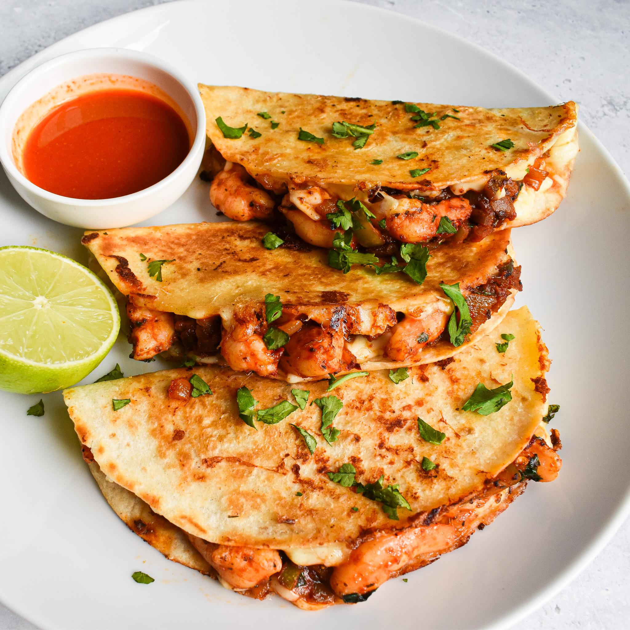3 shrimp quesadilla tacos on a white plate with shot sauce and lime to left of tacos.